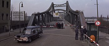 Movie still from “Funeral in Berlin” (1966), directed by Guy Hamilton – A group of people sitting on the side of a bridge; Extreme Wide shot, High angle