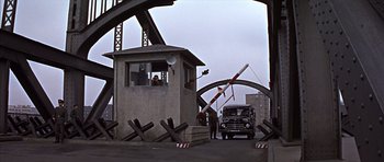Movie still from “Funeral in Berlin” (1966), directed by Guy Hamilton – A man standing next to a truck on a bridge; Wide shot, High angle
