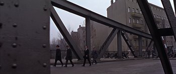 Movie still from “Funeral in Berlin” (1966), directed by Guy Hamilton – A group of men walking across a street under a bridge; Extreme Wide shot, High angle