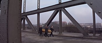 Movie still from “Funeral in Berlin” (1966), directed by Guy Hamilton – A group of men walking across a bridge carrying a casket; Wide shot, High angle