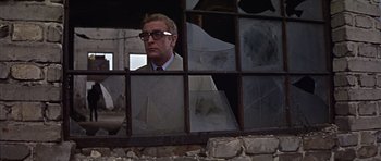 Movie still from “Funeral in Berlin” (1966), directed by Guy Hamilton – A man wearing glasses looking out of a window; Medium shot, Low angle