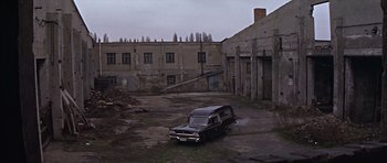 Movie still from “Funeral in Berlin” (1966), directed by Guy Hamilton – An old car parked in an empty lot next to an abandoned building; Extreme Wide shot, High angle