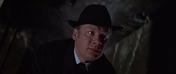 Movie still from “Funeral in Berlin” (1966), directed by Guy Hamilton – A man wearing a black hat and a black suit; Close Up shot, Low angle