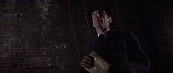 Movie still from “Funeral in Berlin” (1966), directed by Guy Hamilton – A man in a suit and a hat holding a paper bag; Close Up shot, Low angle