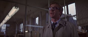 Movie still from “Funeral in Berlin” (1966), directed by Guy Hamilton – A man wearing glasses and wearing a trench coat; Close Up shot, Low angle