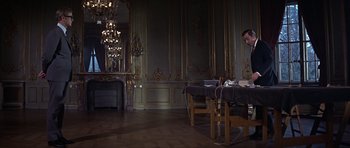 Movie still from “Funeral in Berlin” (1966), directed by Guy Hamilton – A man sitting in front of a laptop computer in a room; Wide shot, Low angle