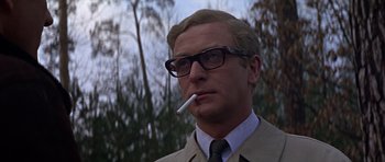Movie still from “Funeral in Berlin” (1966), directed by Guy Hamilton – A man in a suit and glasses smoking a cigarette; Close Up shot, Low angle