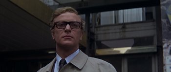 Movie still from “Funeral in Berlin” (1966), directed by Guy Hamilton – A person wearing a suit and glasses; Close Up shot, Low angle