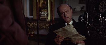 Movie still from “Funeral in Berlin” (1966), directed by Guy Hamilton – An older man in a suit and tie looking at a newspaper; Close Up shot, Low angle