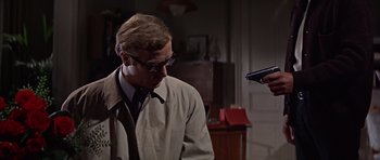 Movie still from “Funeral in Berlin” (1966), directed by Guy Hamilton – A man in a trench coat and glasses holding a gun; Close Up shot, Over the shoulder angle