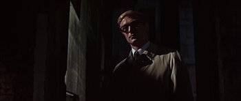 Movie still from “Funeral in Berlin” (1966), directed by Guy Hamilton – A man wearing a suit and tie standing in a dark room; Close Up shot, Low angle