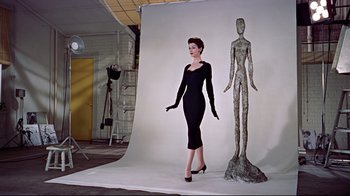 Movie still from “Funny Face” (1957), directed by Stanley Donen – A woman standing next to a statue in a photo studio; Wide shot, Low angle