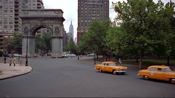 Movie still from “Funny Face” (1957), directed by Stanley Donen – An orange car driving down a street near a tall building; Extreme Wide shot, High angle