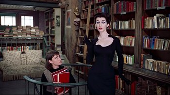 Movie still from “Funny Face” (1957), directed by Stanley Donen – A woman standing in a library next to a woman holding books; Medium shot, Over the shoulder angle