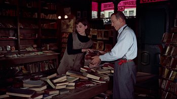 Movie still from “Funny Face” (1957), directed by Stanley Donen – A man and a woman standing next to a pile of books; Medium shot, High angle