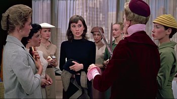 Movie still from “Funny Face” (1957), directed by Stanley Donen – A group of women standing next to each other in a room; Medium shot, Over the shoulder angle