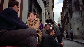 Movie still from “Funny Face” (1957), directed by Stanley Donen – A group of people sitting on the side of a building; Medium shot, Over the shoulder angle