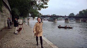 Movie still from “Funny Face” (1957), directed by Stanley Donen – A woman in a trench coat standing next to a body of water; Wide shot, High angle