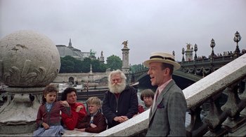 Movie still from “Funny Face” (1957), directed by Stanley Donen – A man in a suit and a hat is talking to a group of people; Medium shot, Over the shoulder angle