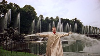 Movie still from “Funny Face” (1957), directed by Stanley Donen – A man standing in front of a fountain with his arms outstretched; Wide shot, Low angle