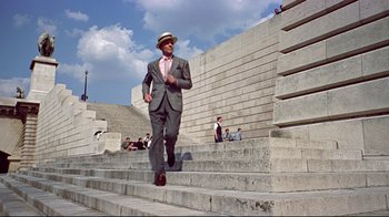 Movie still from “Funny Face” (1957), directed by Stanley Donen – A man in a suit and hat walking down the stairs; Wide shot, Low angle