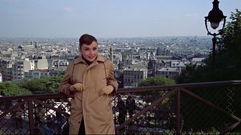 Movie still from “Funny Face” (1957), directed by Stanley Donen – A woman in a trench coat standing in front of a city; Medium shot, Over the shoulder angle
