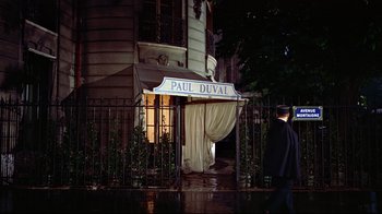 Movie still from “Funny Face” (1957), directed by Stanley Donen – A man walking in front of a building at night; Wide shot, Over the shoulder angle