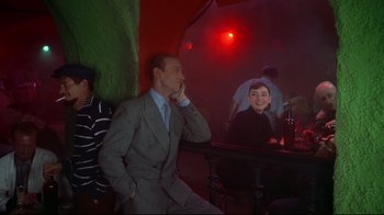 Movie still from “Funny Face” (1957), directed by Stanley Donen – A group of people sitting at a table in a room; Medium shot, Over the shoulder angle