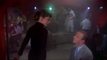 Movie still from “Funny Face” (1957), directed by Stanley Donen – A man and a woman are standing in front of a crowd; Medium shot, Low angle