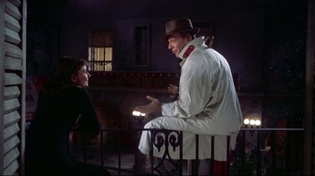 Movie still from “Funny Face” (1957), directed by Stanley Donen – A man wearing a hat and a white coat talking to a boy; Medium shot, Over the shoulder angle