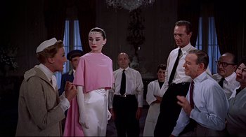 Movie still from “Funny Face” (1957), directed by Stanley Donen – A group of people standing next to each other in a room; Medium shot, Over the shoulder angle