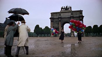 Movie still from “Funny Face” (1957), directed by Stanley Donen – A group of people standing in front of an archway holding balloons; Wide shot, Low angle