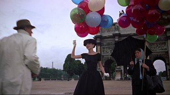 Movie still from “Funny Face” (1957), directed by Stanley Donen – A woman in a black dress holding up her hand; Wide shot, Low angle