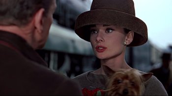 Movie still from “Funny Face” (1957), directed by Stanley Donen – A woman wearing a brown hat with a dog in front of her; Close Up shot, Over the shoulder angle