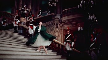 Movie still from “Funny Face” (1957), directed by Stanley Donen – A woman in a green dress is walking down the stairs; Wide shot, Low angle
