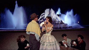 Movie still from “Funny Face” (1957), directed by Stanley Donen – A man and a woman dressed up in front of a fountain at night; Medium shot, Over the shoulder angle