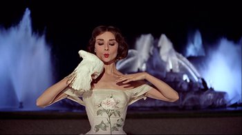 Movie still from “Funny Face” (1957), directed by Stanley Donen – A woman in a white dress holding a white bird in her hands; Medium shot, Low angle