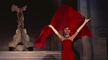 Movie still from “Funny Face” (1957), directed by Stanley Donen – A woman in a long red dress holding a red cloth; Medium shot, Low angle