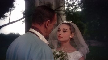 Movie still from “Funny Face” (1957), directed by Stanley Donen – A man and a woman standing next to each other in front of a tree; Close Up shot, Over the shoulder angle