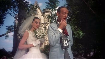 Movie still from “Funny Face” (1957), directed by Stanley Donen – A man and a woman standing next to each other in front of a building; Medium shot, Low angle