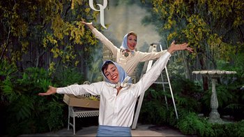 Movie still from “Funny Face” (1957), directed by Stanley Donen – A couple of women standing next to each other in front of trees; Medium shot, Low angle