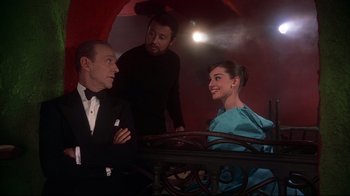 Movie still from “Funny Face” (1957), directed by Stanley Donen – Two men and a woman sitting at a dinner table; Medium shot, Over the shoulder angle