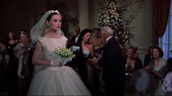 Movie still from “Funny Face” (1957), directed by Stanley Donen – A woman in a white dress holding a bouquet of flowers; Medium shot, Over the shoulder angle