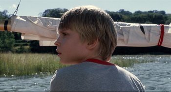 Movie still from “Funny Games” (2007), directed by Michael Haneke – A young boy sitting in front of a body of water; Close Up shot, Over the shoulder angle