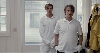 Movie still from “Funny Games” (2007), directed by Michael Haneke – Two young men in white shirts standing next to each other in front of a window; Medium shot, Low angle