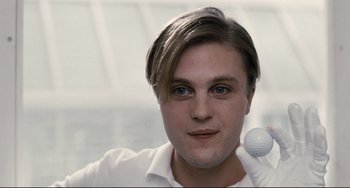 Movie still from “Funny Games” (2007), directed by Michael Haneke – A young man holding a golf ball in one hand and a golf club in the other; Close Up shot, Low angle