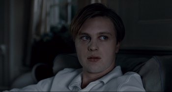 Movie still from “Funny Games” (2007), directed by Michael Haneke – A young man sitting in a chair looking into the camera; Close Up shot, Over the shoulder angle