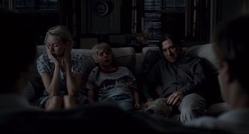 Movie still from “Funny Games” (2007), directed by Michael Haneke – Two adults and a child sitting on a couch watching television; Medium shot, Over the shoulder angle