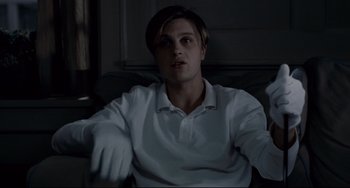 Movie still from “Funny Games” (2007), directed by Michael Haneke – A man sitting on a couch in the dark; Medium shot, Low angle