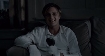 Movie still from “Funny Games” (2007), directed by Michael Haneke – A man sitting on a couch holding a remote control; Medium shot, High angle